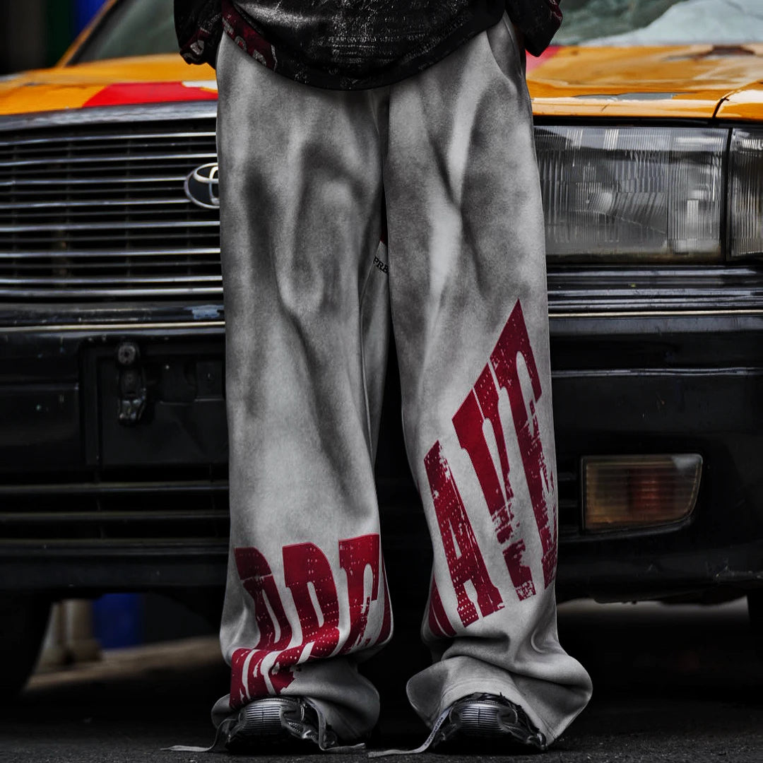 Sanhoostudio sweatpants featuring distressed letter graphics and fleece lining for warmth. Designed with an oversized wide leg fit for unisex vintage-inspired streetwear styling.