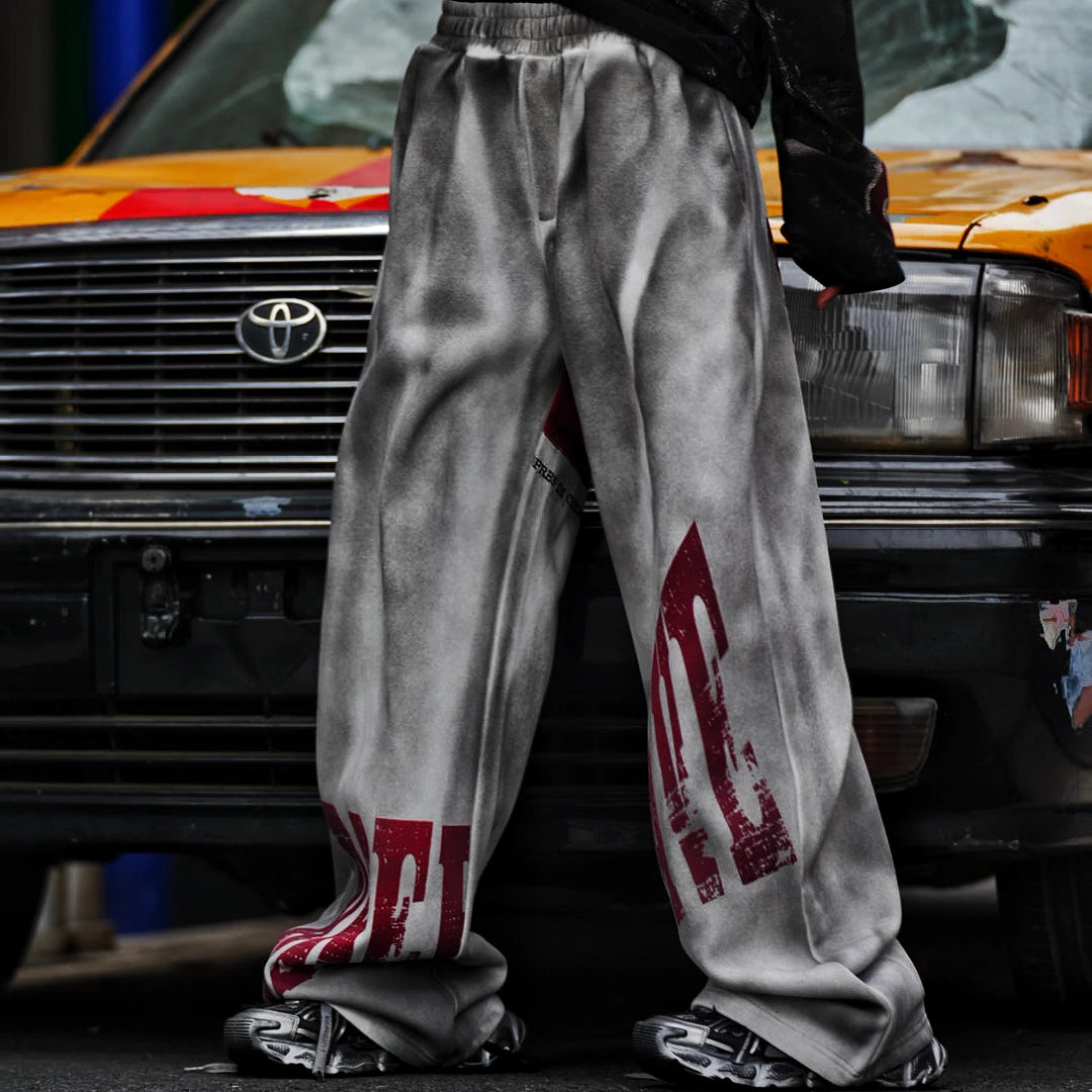 Sanhoostudio sweatpants featuring distressed letter graphics and fleece lining for warmth. Designed with an oversized wide leg fit for unisex vintage-inspired streetwear styling.