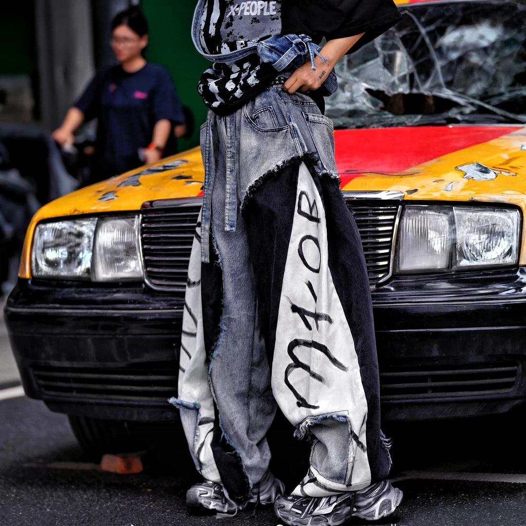 Sanhoostudio denim pants featuring distressed washed finish, patchwork detailing, and wide leg scythe-cut silhouette. Designed for modern streetwear styling with relaxed comfort and versatile everyday wear.