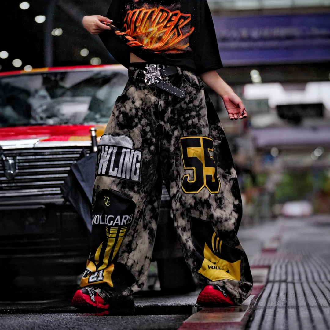 Sanhoostudio denim pants featuring patchwork applique details, distressed wash treatment, and a wide leg scythe-cut silhouette. Designed for contemporary streetwear styling with relaxed comfort and standout visual structure.