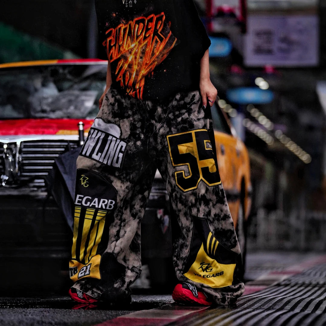 Sanhoostudio denim pants featuring patchwork applique details, distressed wash treatment, and a wide leg scythe-cut silhouette. Designed for contemporary streetwear styling with relaxed comfort and standout visual structure.