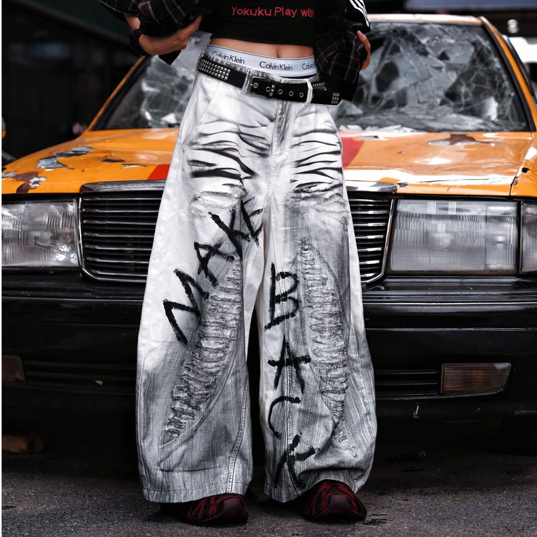 Sanhoostudio white denim pants featuring distressed ripped details, spray-paint artwork, and a wide leg scythe-cut silhouette. Designed for contemporary streetwear styling with comfort and bold visual character.