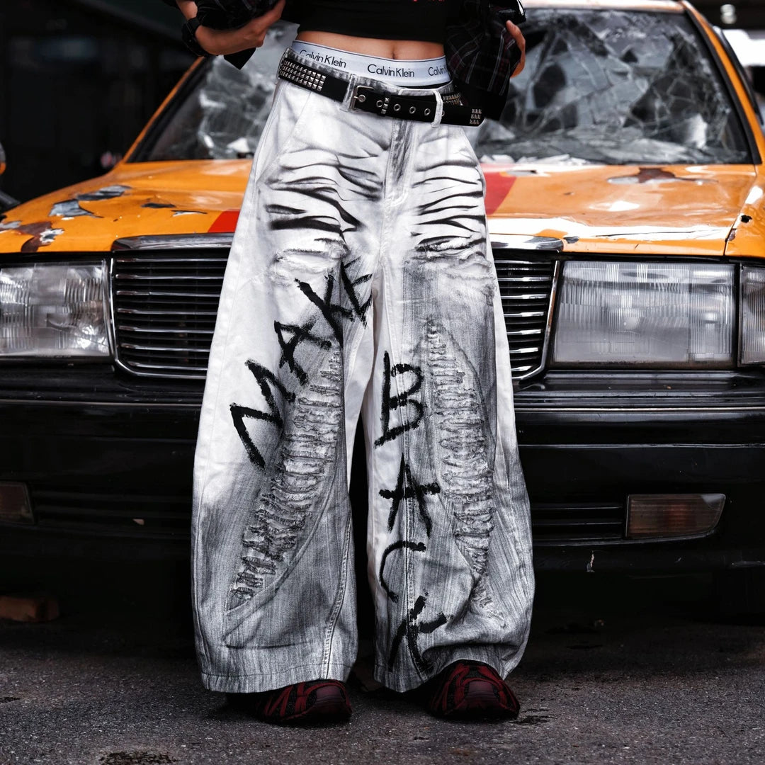 Sanhoostudio white denim pants featuring distressed ripped details, spray-paint artwork, and a wide leg scythe-cut silhouette. Designed for contemporary streetwear styling with comfort and bold visual character.