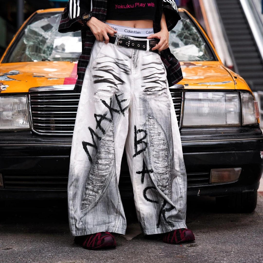 Sanhoostudio white denim pants featuring distressed ripped details, spray-paint artwork, and a wide leg scythe-cut silhouette. Designed for contemporary streetwear styling with comfort and bold visual character.
