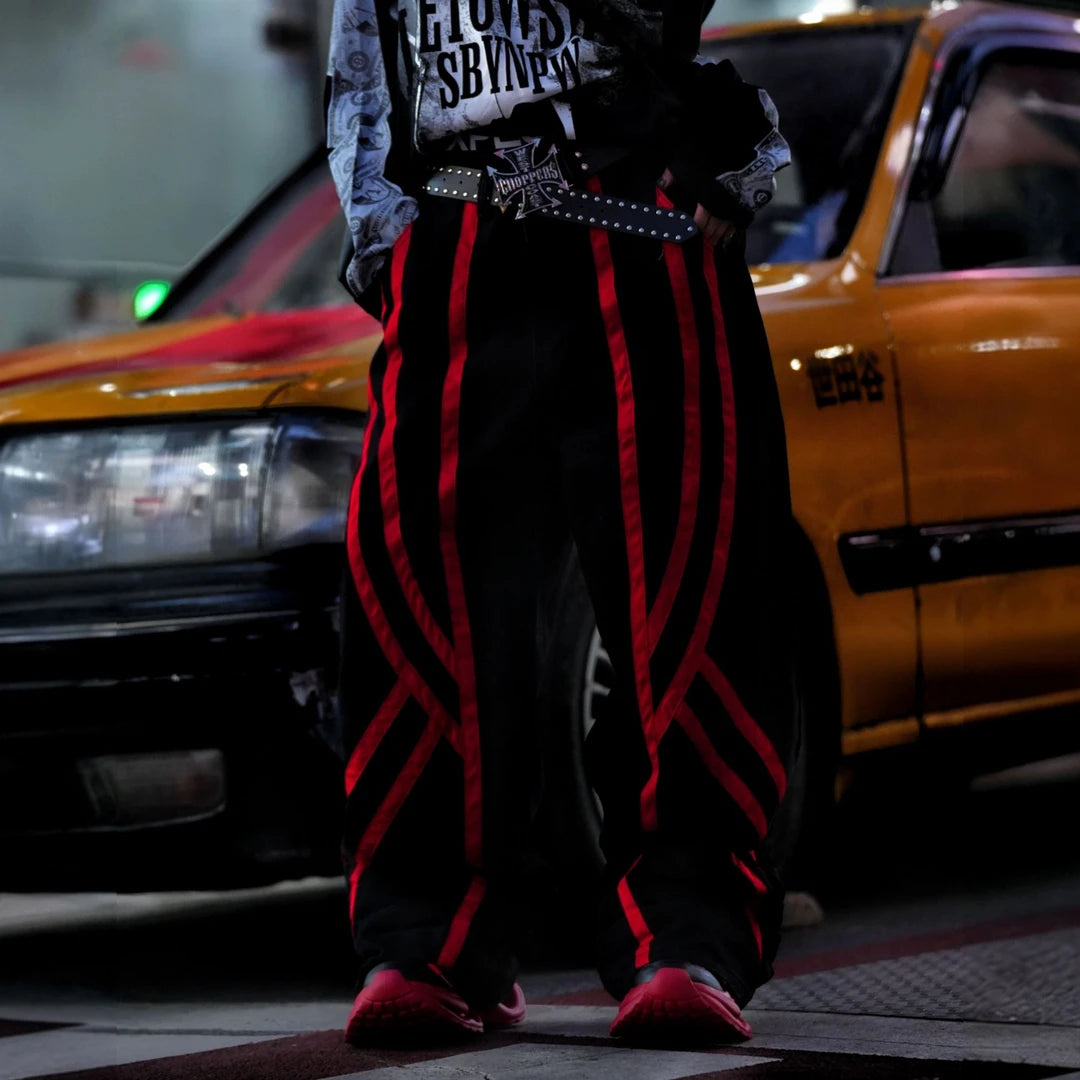 Sanhoostudio denim pants featuring distinctive red line detailing, heavyweight washed construction, distressed effects, and patchwork elements with a wide leg scythe silhouette. Designed for bold streetwear styling with relaxed comfort, strong visual structure, and versatile everyday wear.