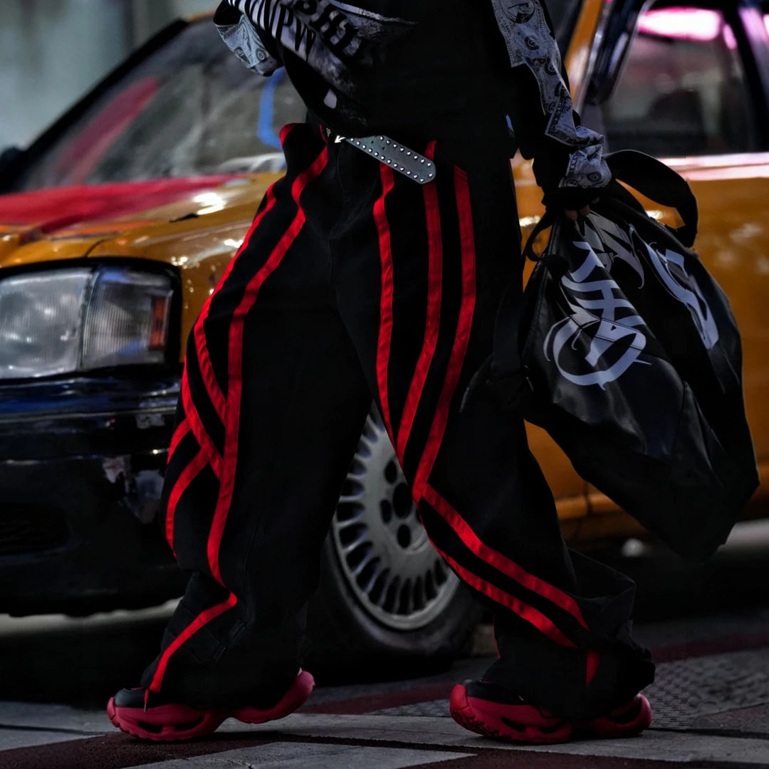 Sanhoostudio denim pants featuring distinctive red line detailing, heavyweight washed construction, distressed effects, and patchwork elements with a wide leg scythe silhouette. Designed for bold streetwear styling with relaxed comfort, strong visual structure, and versatile everyday wear.