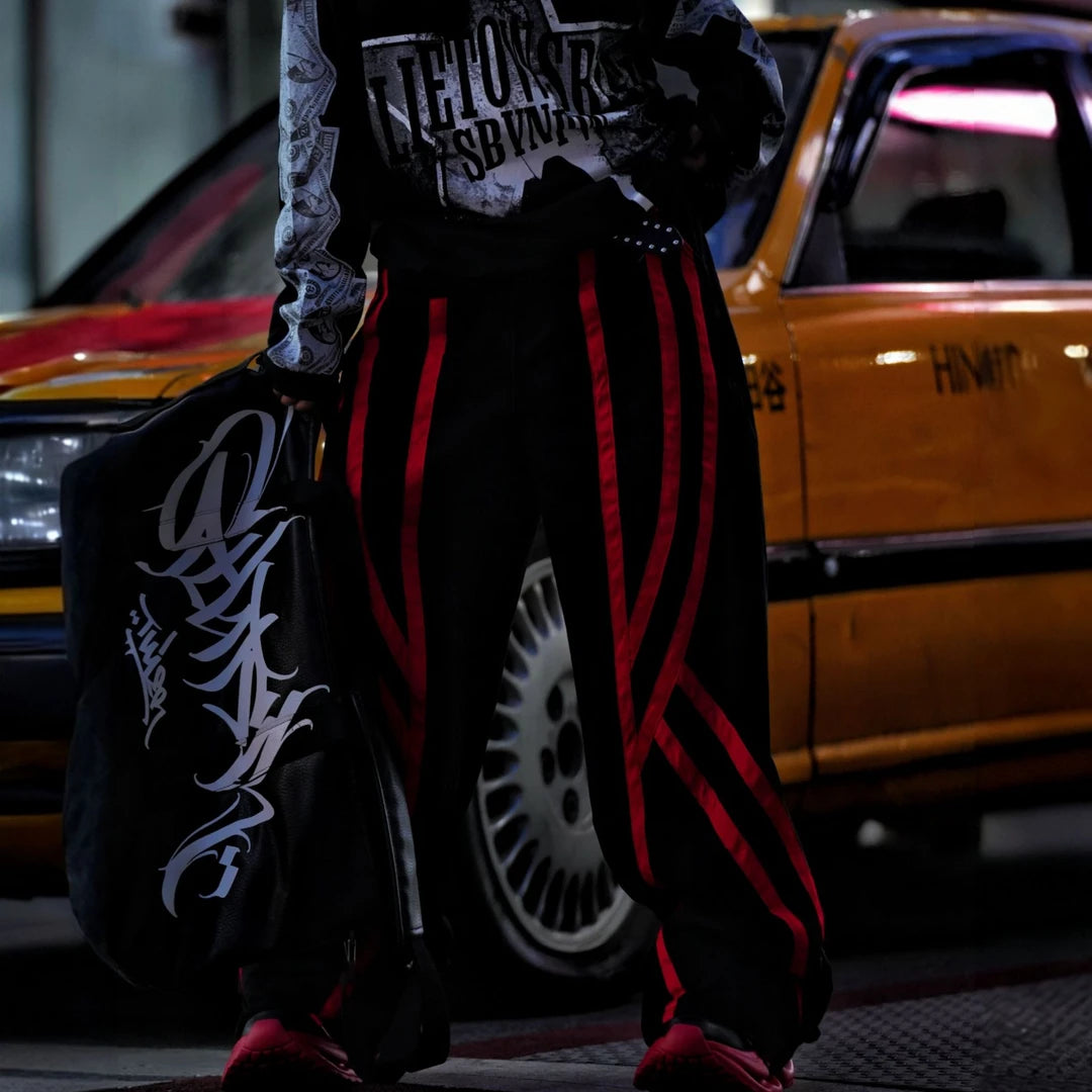 Sanhoostudio denim pants featuring distinctive red line detailing, heavyweight washed construction, distressed effects, and patchwork elements with a wide leg scythe silhouette. Designed for bold streetwear styling with relaxed comfort, strong visual structure, and versatile everyday wear.