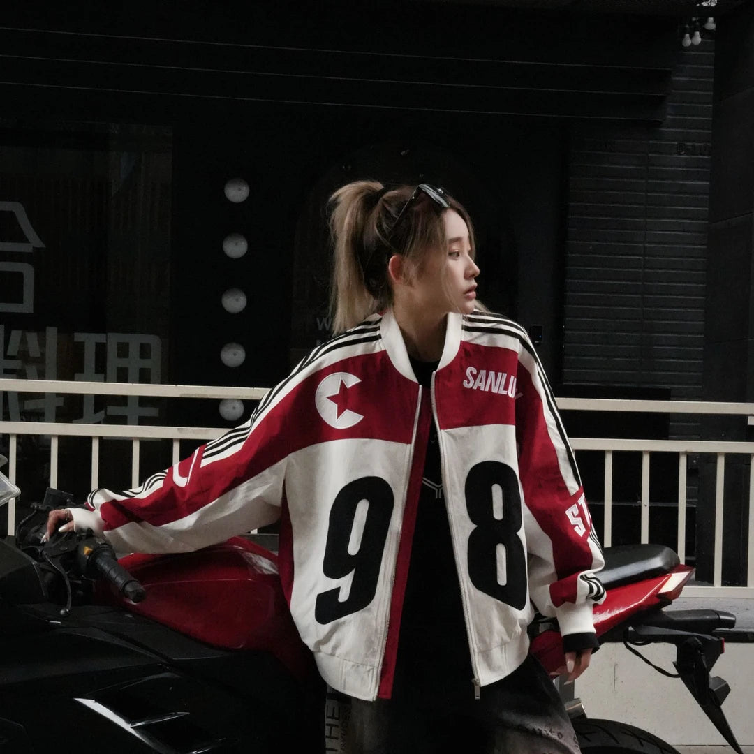 Sanhoostudio bomber jacket featuring black and white colorblock panels, number and letter graphics, a zip-up front, and a cropped racing-inspired silhouette. Designed for early fall streetwear with sporty motorcycle character and versatile everyday layering.