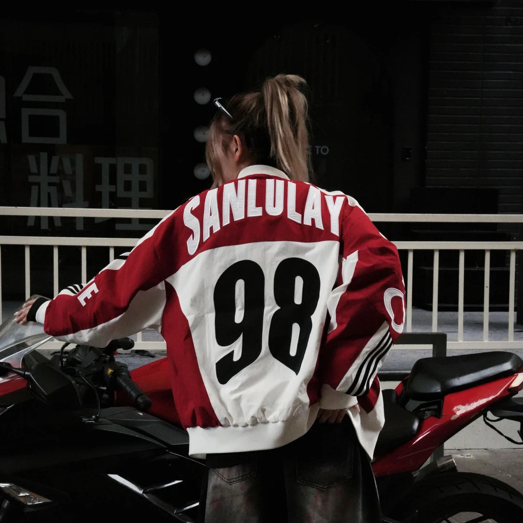 Sanhoostudio bomber jacket featuring black and white colorblock panels, number and letter graphics, a zip-up front, and a cropped racing-inspired silhouette. Designed for early fall streetwear with sporty motorcycle character and versatile everyday layering.