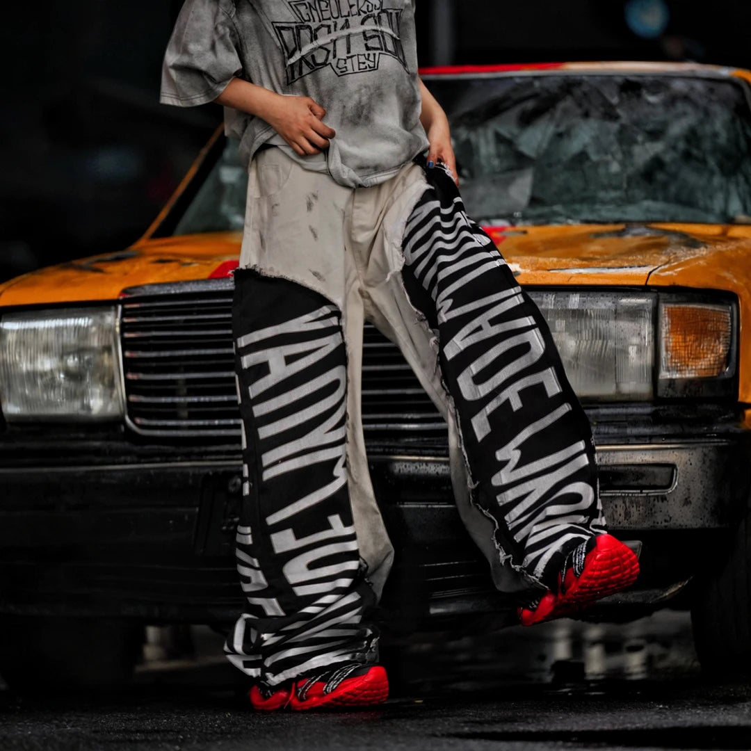 Sanhoostudio denim pants featuring asymmetric panel construction, distressed washed detailing, and a relaxed wide leg scythe silhouette. Designed for lightweight seasonal streetwear styling with distinctive patchwork structure, comfortable movement, and bold contemporary urban appeal.
