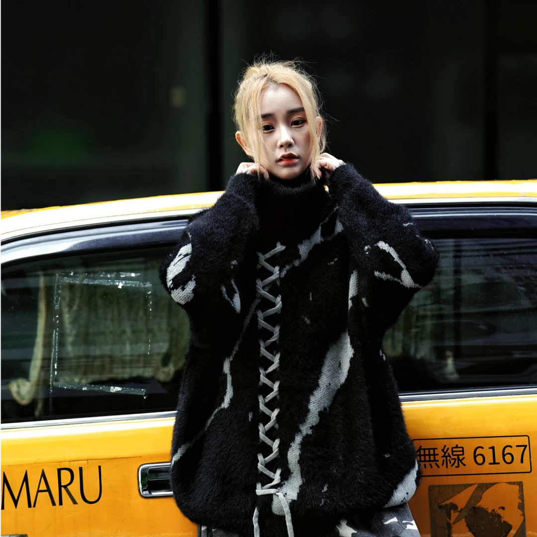 Sanhoostudio knit sweater featuring gothic-inspired lace-up detailing, a structured stand collar, heavyweight knitted construction, and a relaxed oversized silhouette. Designed for fall and winter streetwear styling with comfortable warmth, distinctive dark aesthetics, and versatile layering.
