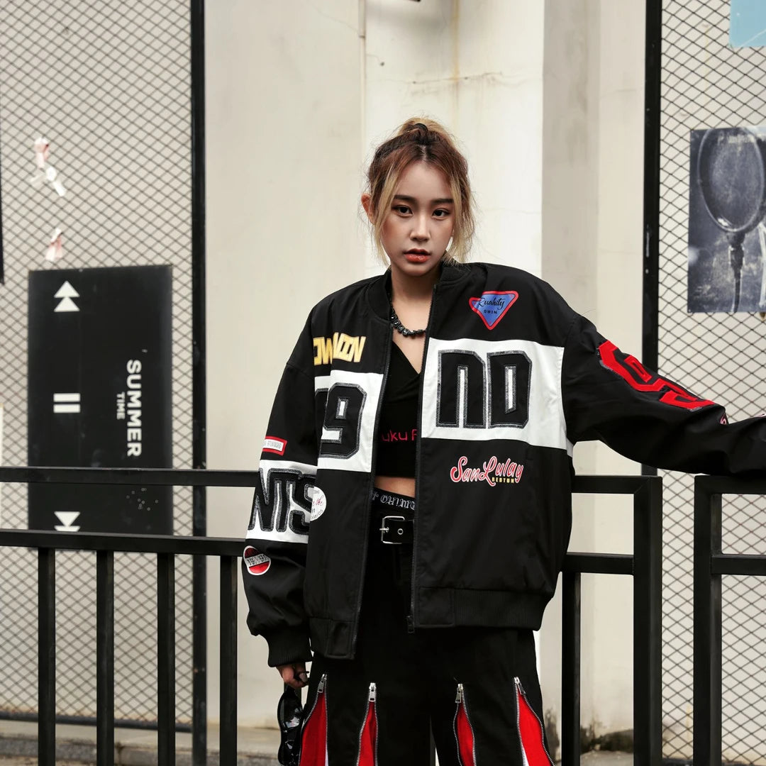Sanhoostudio padded varsity jacket featuring bold colorblock patchwork, shimmering sequin detailing, and racing-inspired design elements. Designed for statement streetwear styling with comfortable insulation, a relaxed silhouette, distinctive motorsport aesthetics, and eye-catching visual appeal.