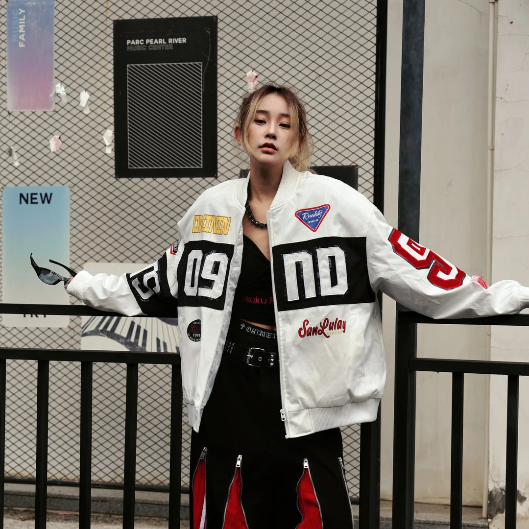 Sanhoostudio padded varsity jacket featuring bold colorblock patchwork, shimmering sequin detailing, and racing-inspired design elements. Designed for statement streetwear styling with comfortable insulation, a relaxed silhouette, distinctive motorsport aesthetics, and eye-catching visual appeal.