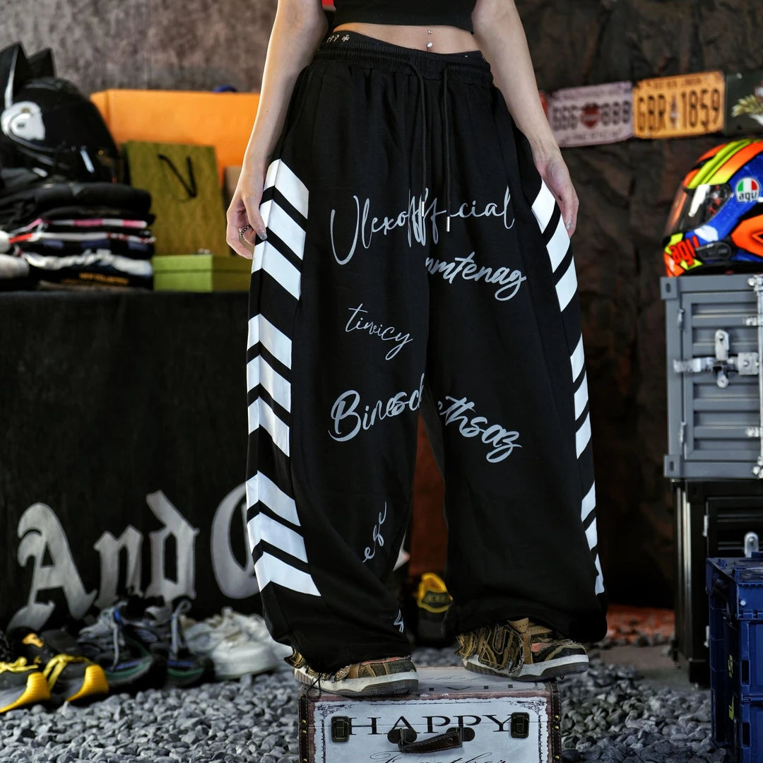 Sanhoostudio sweatpants featuring vintage American-inspired letter graphics, an adjustable drawstring waistband, and a relaxed wide leg silhouette. Designed for contemporary streetwear styling with comfortable casual construction, oversized proportions, retro athletic character, and versatile everyday appeal.