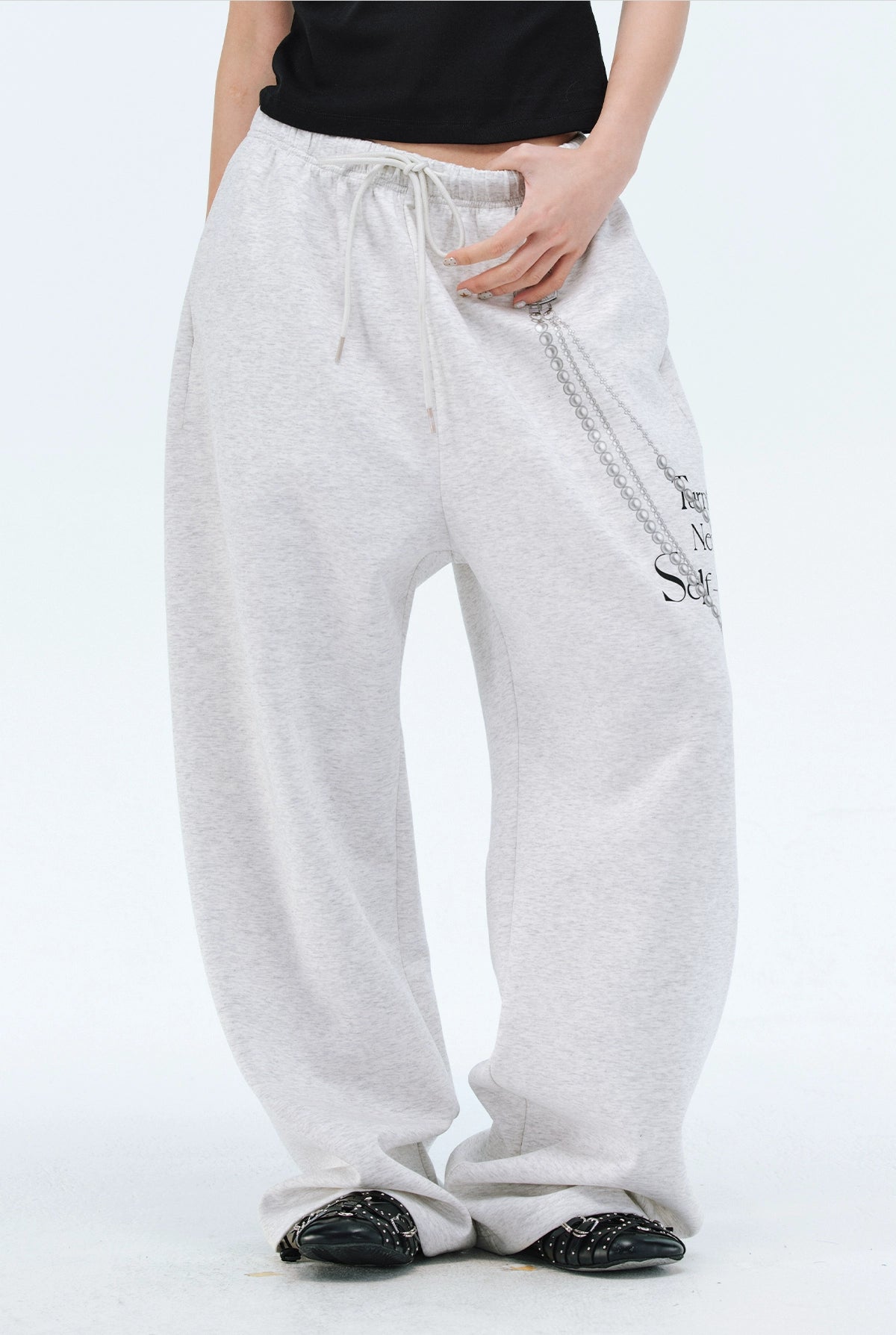 These Sanhoostudio pants stand out with pearl chain embellishments and bold slogan prints, merging casual comfort with high street individuality. Designed with a relaxed fit, they highlight a balance of playful accessories and edgy fashion vibes.