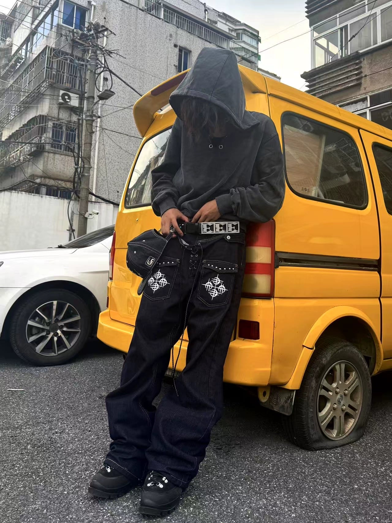 The Sanhoostudio double-waist jeans showcase a unique studded drawstring design with blade-cut legs. Their deconstructed silhouette and washed finish bring punk-inspired energy to everyday streetwear styling, making them a bold wardrobe choice.