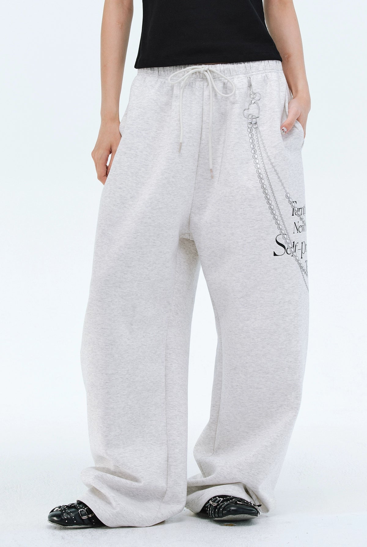 These Sanhoostudio pants stand out with pearl chain embellishments and bold slogan prints, merging casual comfort with high street individuality. Designed with a relaxed fit, they highlight a balance of playful accessories and edgy fashion vibes.