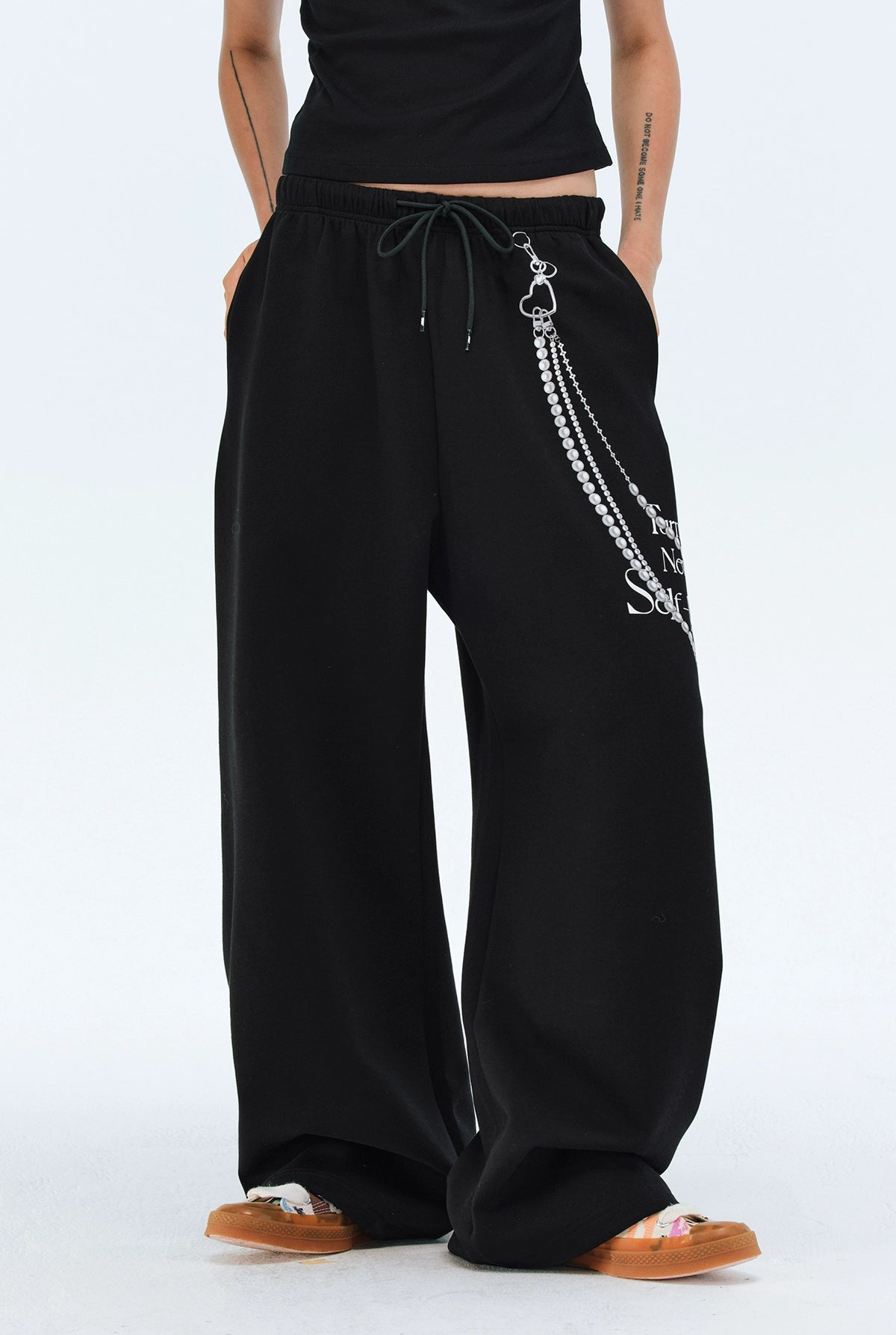 These Sanhoostudio pants stand out with pearl chain embellishments and bold slogan prints, merging casual comfort with high street individuality. Designed with a relaxed fit, they highlight a balance of playful accessories and edgy fashion vibes.