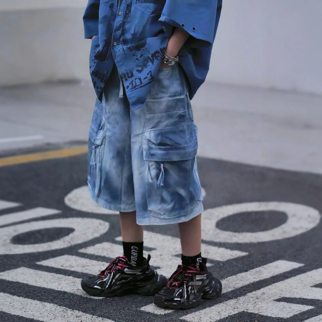 Sanhoostudio cargo shorts featuring tie dye finish, multi-pocket design, and relaxed wide leg fit. Built for summer streetwear styling with breathable comfort, lightweight feel, and functional everyday wear.