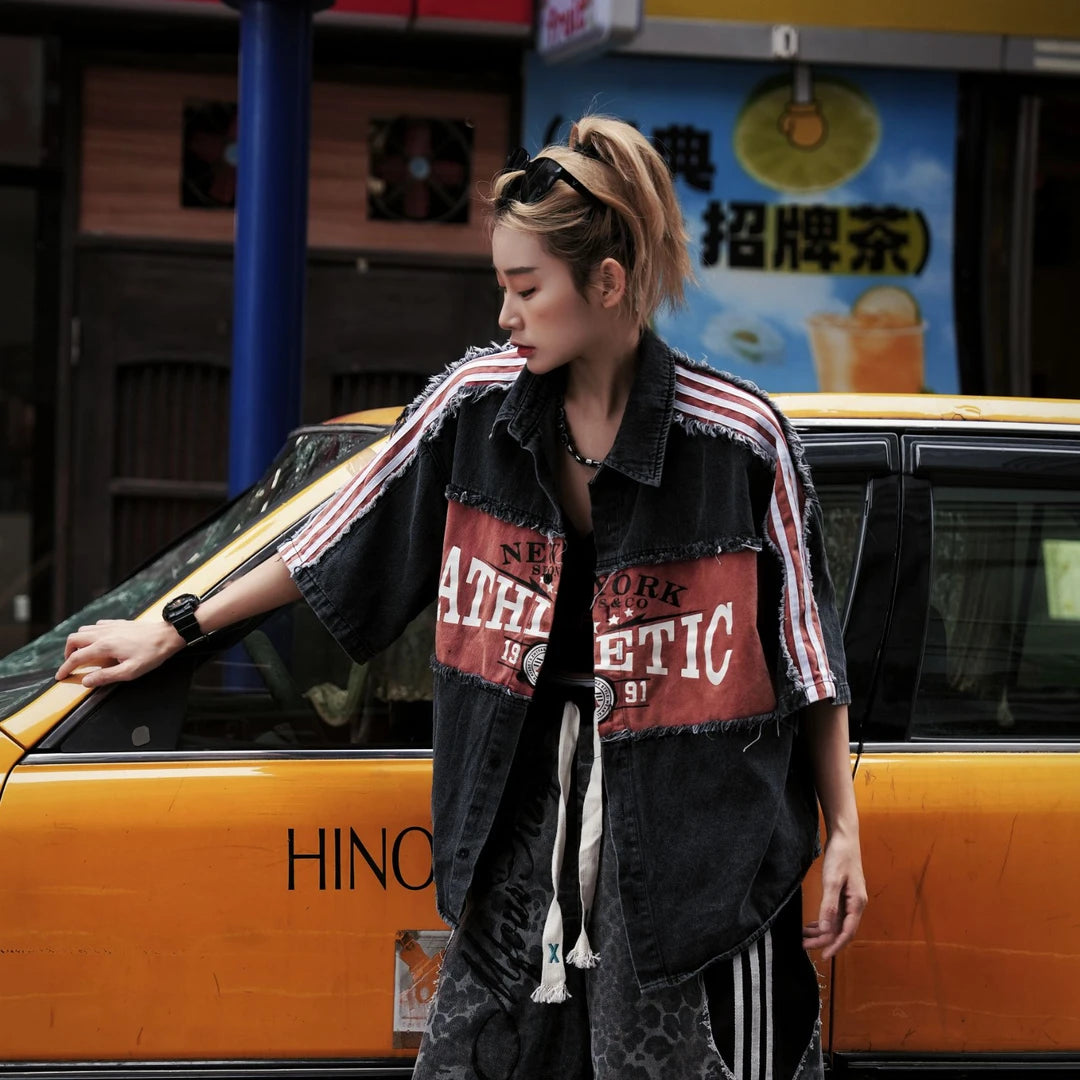 Sanhoostudio denim short sleeve shirt featuring patchwork construction, fringe detailing, and letter-inspired design elements. Built for creative streetwear outfits with a relaxed fit and standout visual appeal.