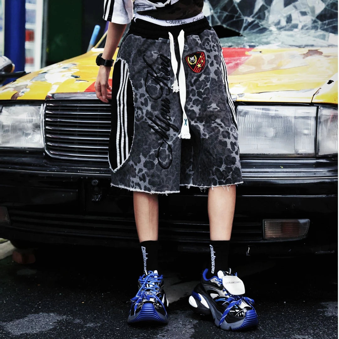 Sanhoostudio shorts featuring leopard print detailing, embroidered accents, and a relaxed scythe-inspired silhouette. Designed for summer streetwear styling with comfort, mobility, and bold visual impact.