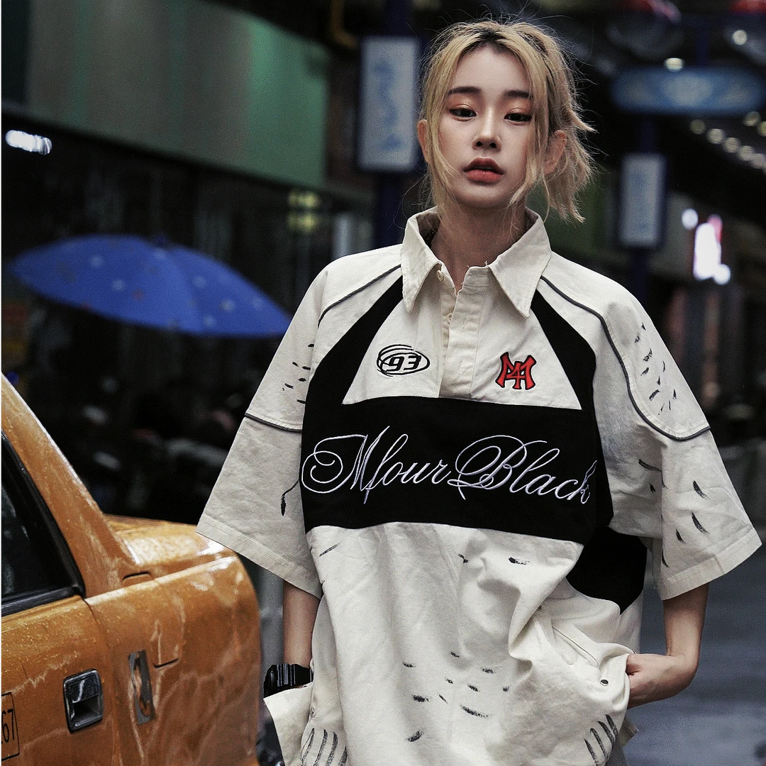 Sanhoostudio polo shirt featuring colorblock stripe detailing, letter-inspired accents, and a relaxed oversized fit. Designed for versatile summer outfits that blend casual comfort with modern streetwear aesthetics.