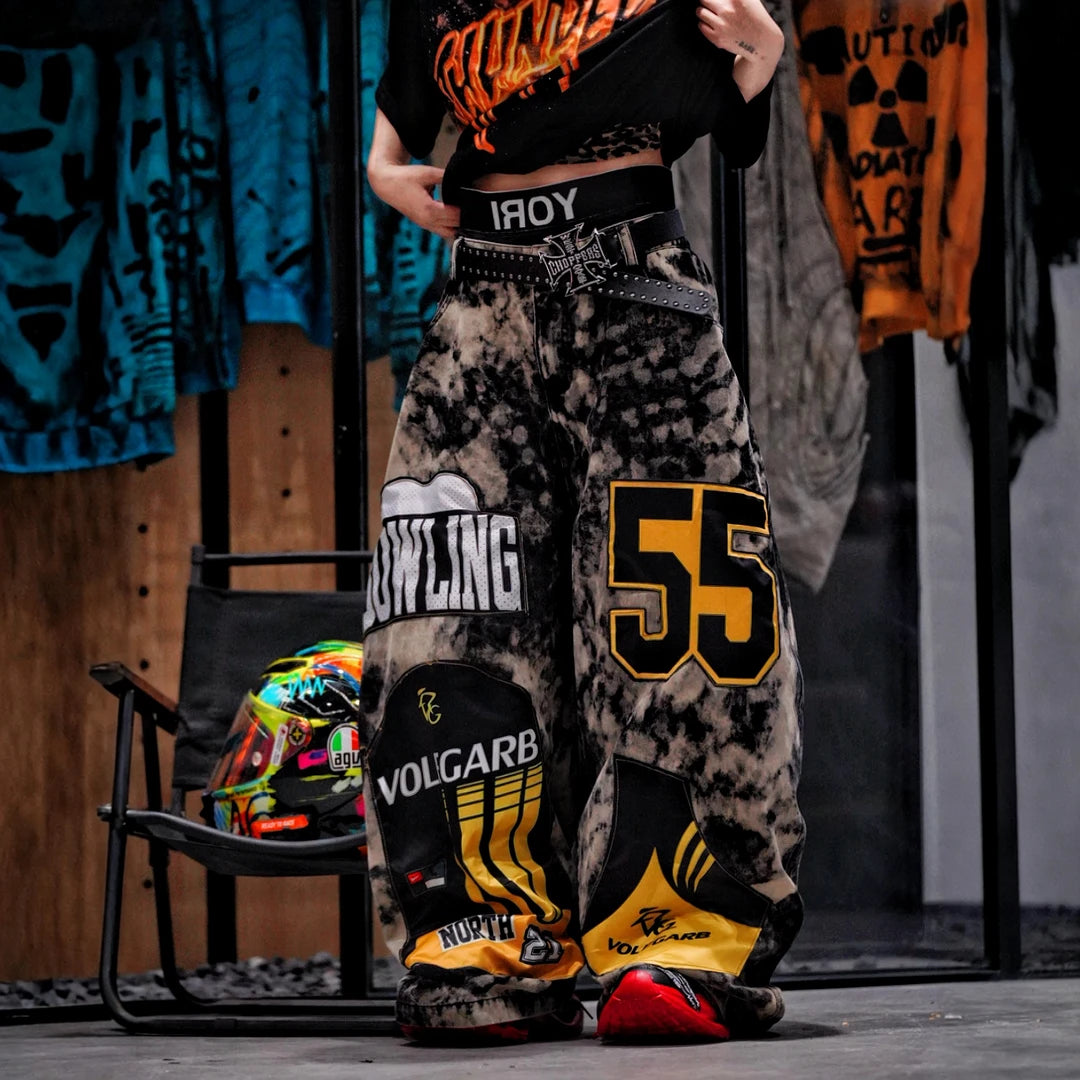 Sanhoostudio denim pants featuring patchwork applique details, distressed wash treatment, and a wide leg scythe-cut silhouette. Designed for contemporary streetwear styling with relaxed comfort and standout visual structure.