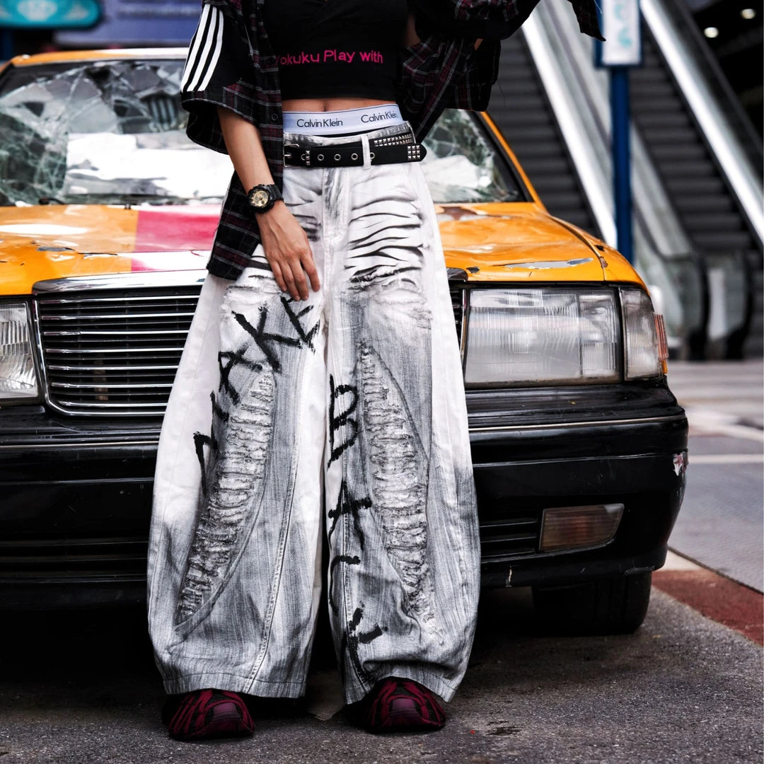 Sanhoostudio white denim pants featuring distressed ripped details, spray-paint artwork, and a wide leg scythe-cut silhouette. Designed for contemporary streetwear styling with comfort and bold visual character.