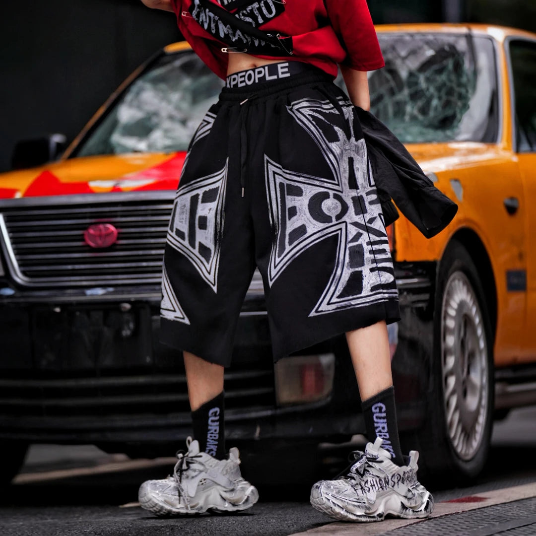 Sanhoostudio shorts featuring distressed wash treatment, graffiti detailing, and cross-inspired design elements with a relaxed fit. Built for summer streetwear outfits with breathable comfort and versatile styling appeal.