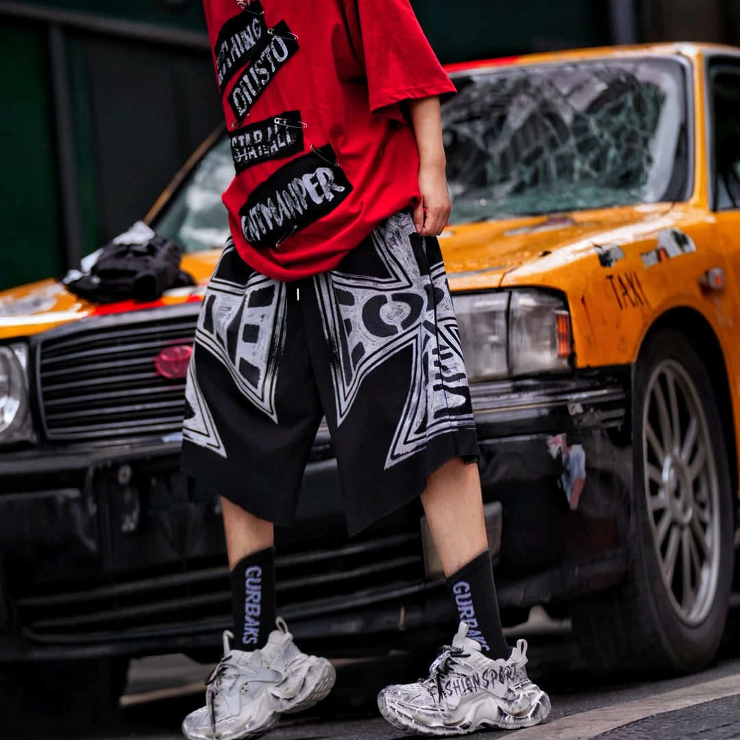 Sanhoostudio shorts featuring distressed wash treatment, graffiti detailing, and cross-inspired design elements with a relaxed fit. Built for summer streetwear outfits with breathable comfort and versatile styling appeal.