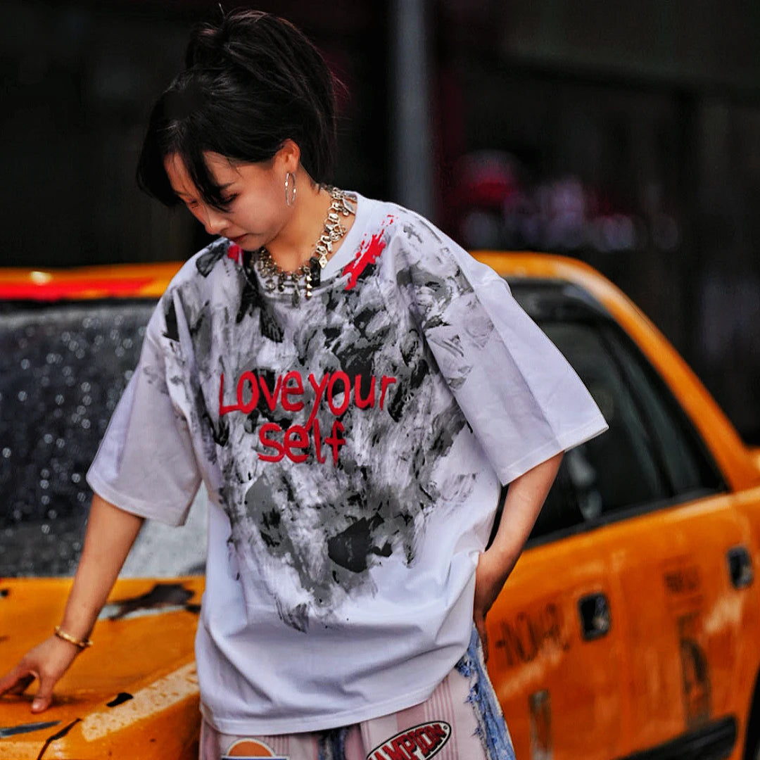 Sanhoostudio short sleeve T-shirt featuring abstract spray-print artwork, breathable fabric construction, and a relaxed oversized fit. Designed for modern streetwear styling with lightweight comfort, bold graphic appeal, and versatile summer wear.