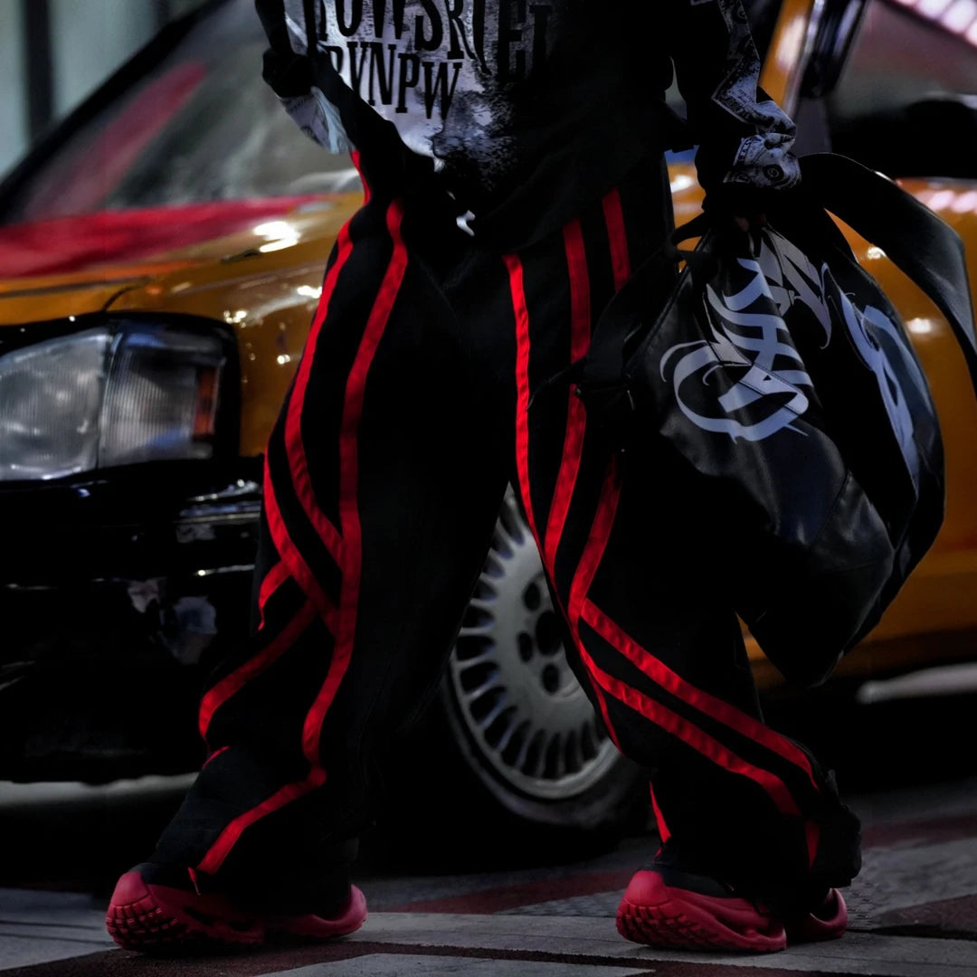 Sanhoostudio denim pants featuring distinctive red line detailing, heavyweight washed construction, distressed effects, and patchwork elements with a wide leg scythe silhouette. Designed for bold streetwear styling with relaxed comfort, strong visual structure, and versatile everyday wear.