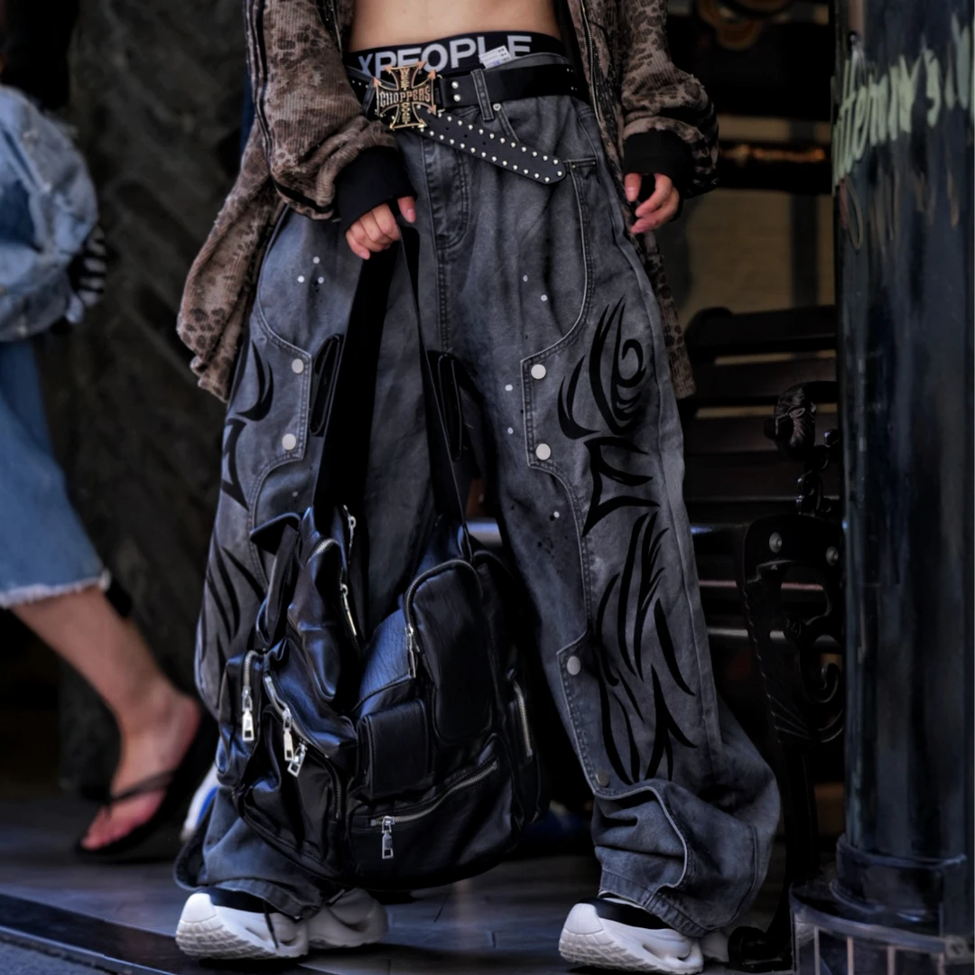 Sanhoostudio denim pants featuring grey and black totem-inspired detailing, heavyweight washed construction, distressed effects, and patchwork elements with a wide leg scythe silhouette. Designed for bold streetwear styling with relaxed comfort and distinctive urban character.