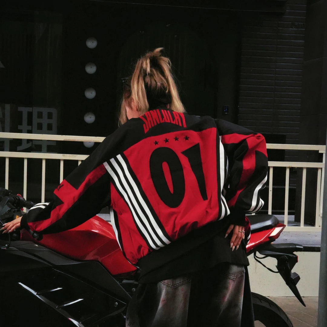 Sanhoostudio varsity jacket featuring red and black colorblock construction, number applique embroidery, striped detailing, and a relaxed oversized fit. Inspired by vintage racing and varsity aesthetics for bold fall streetwear styling and comfortable everyday wear.