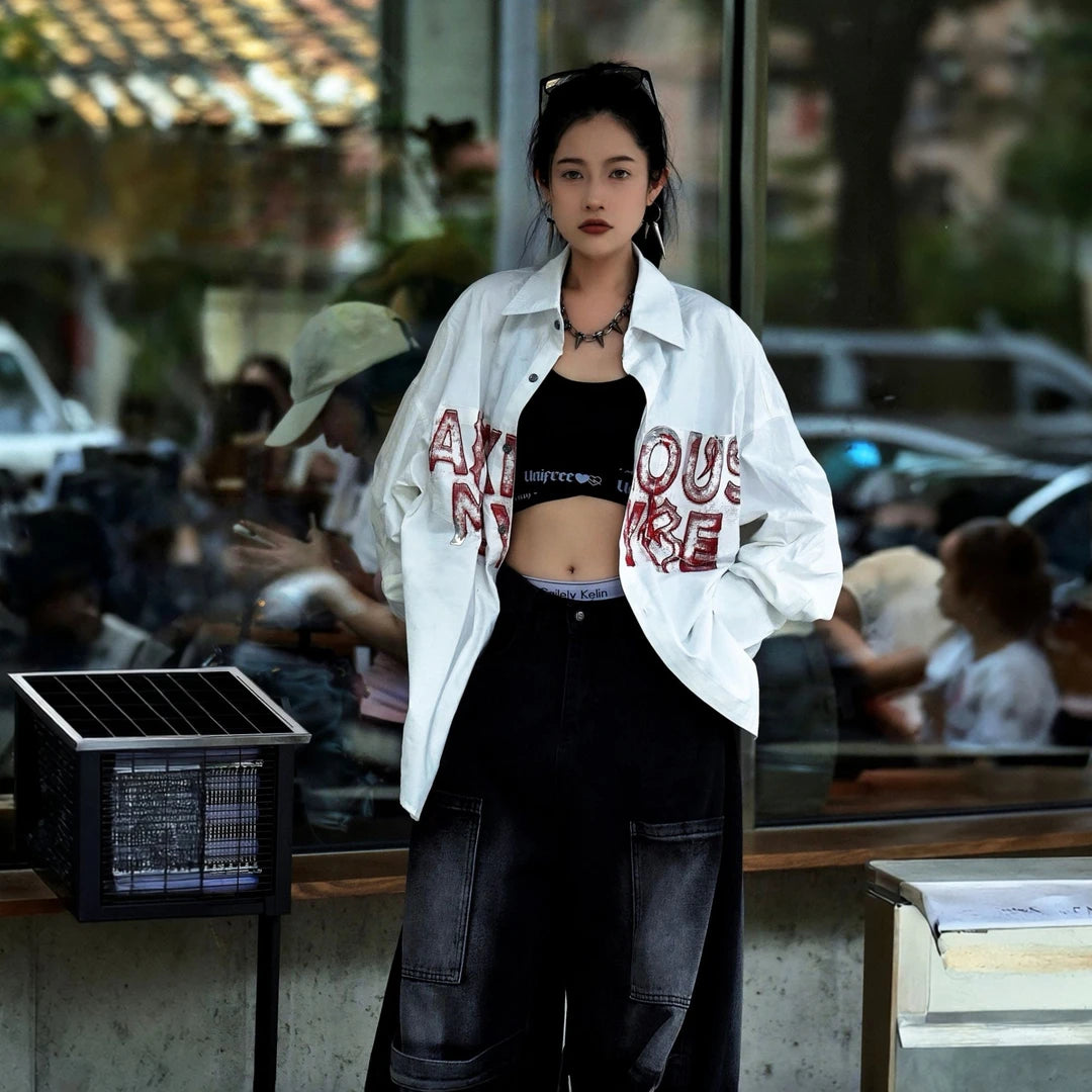 Sanhoostudio long sleeve shirt featuring metallic-effect letter detailing, relaxed dropped shoulders, and an oversized silhouette. Designed for dark high-street styling with bold visual texture, comfortable layering, and a sleek urban aesthetic for versatile everyday outfits.
