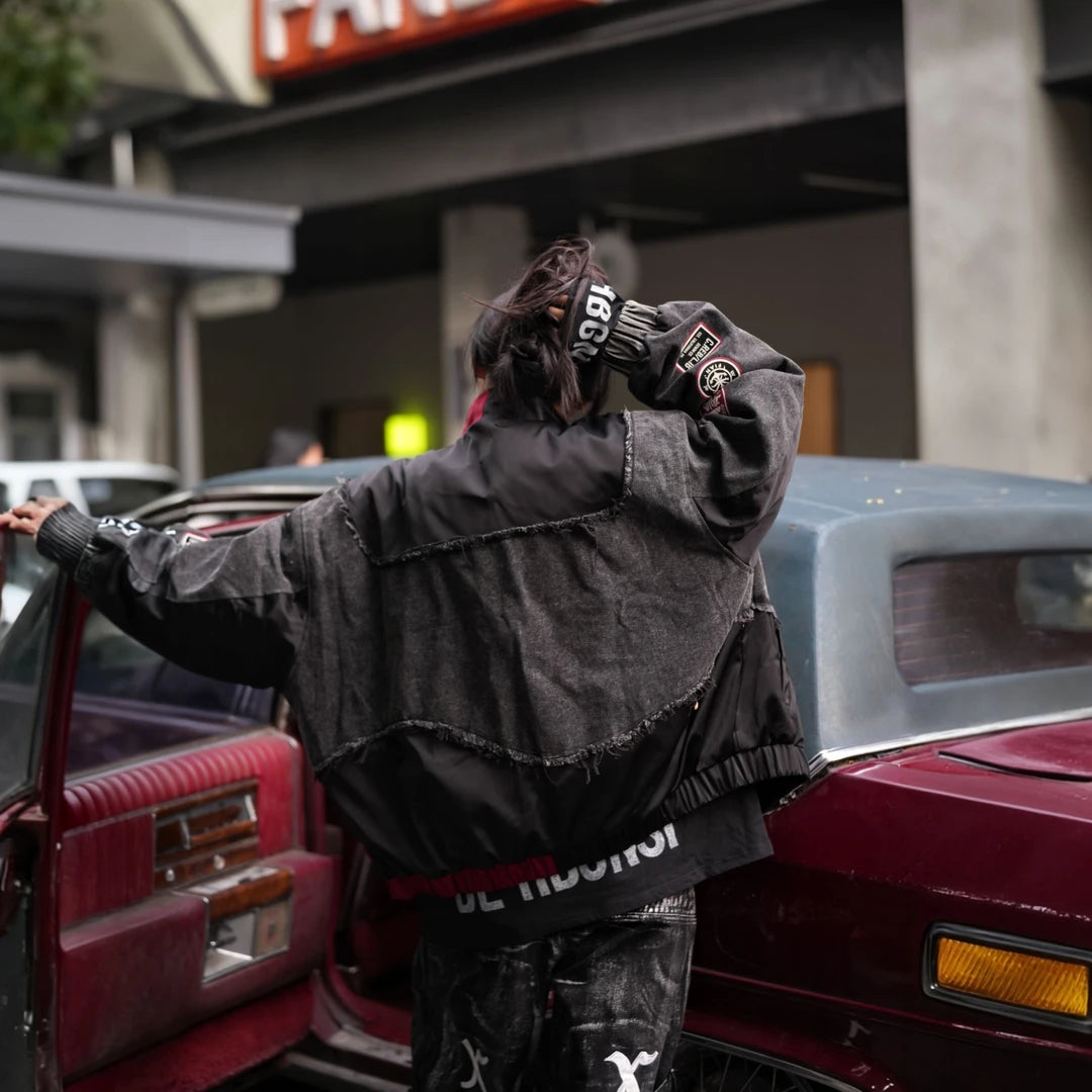 Sanhoostudio denim jacket featuring black patch applique embroidery, distressed surface detailing, and a relaxed oversized silhouette with added seasonal warmth. Designed for statement streetwear layering with rugged texture, handcrafted character, and versatile urban styling.