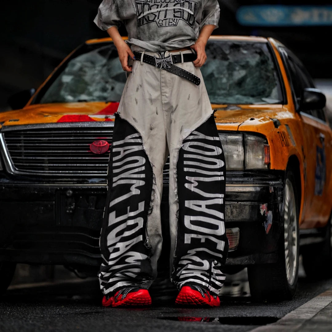 Sanhoostudio denim pants featuring asymmetric panel construction, distressed washed detailing, and a relaxed wide leg scythe silhouette. Designed for lightweight seasonal streetwear styling with distinctive patchwork structure, comfortable movement, and bold contemporary urban appeal.