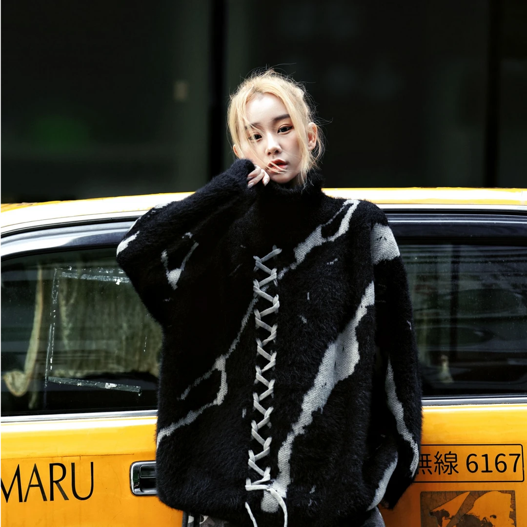 Sanhoostudio knit sweater featuring gothic-inspired lace-up detailing, a structured stand collar, heavyweight knitted construction, and a relaxed oversized silhouette. Designed for fall and winter streetwear styling with comfortable warmth, distinctive dark aesthetics, and versatile layering.