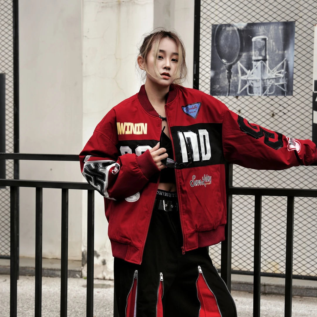 Sanhoostudio padded varsity jacket featuring bold colorblock patchwork, shimmering sequin detailing, and racing-inspired design elements. Designed for statement streetwear styling with comfortable insulation, a relaxed silhouette, distinctive motorsport aesthetics, and eye-catching visual appeal.