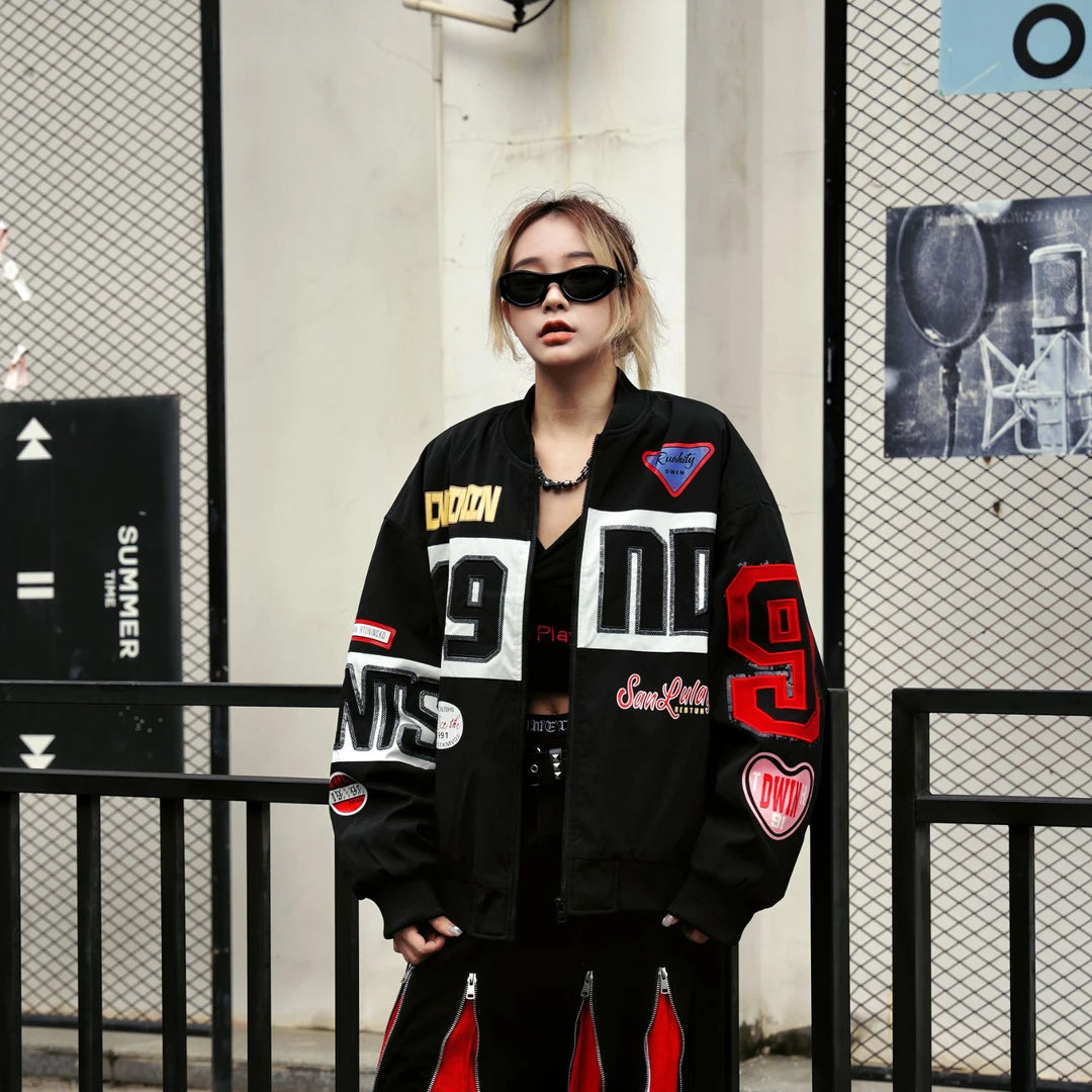 Sanhoostudio padded varsity jacket featuring bold colorblock patchwork, shimmering sequin detailing, and racing-inspired design elements. Designed for statement streetwear styling with comfortable insulation, a relaxed silhouette, distinctive motorsport aesthetics, and eye-catching visual appeal.