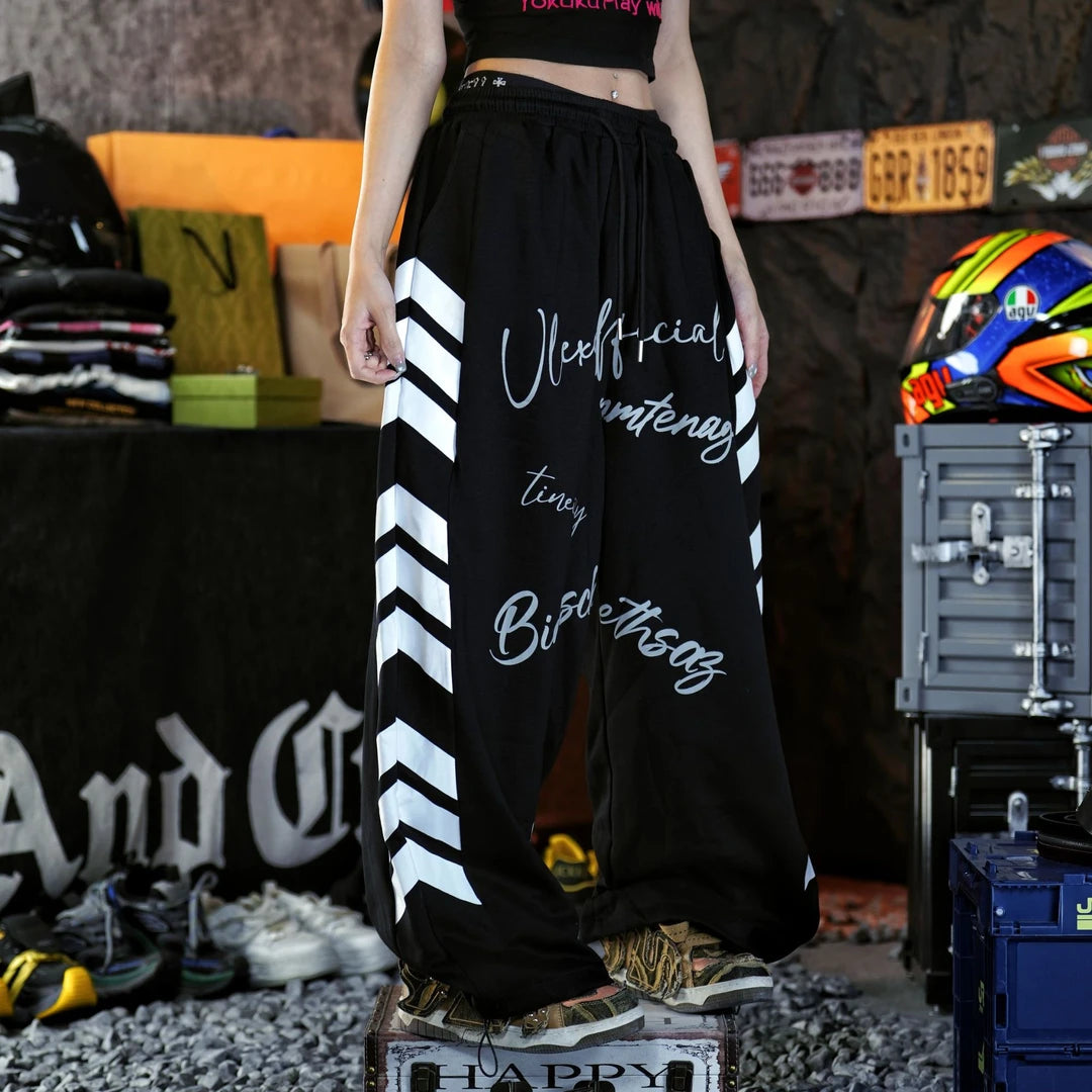 Sanhoostudio sweatpants featuring vintage American-inspired letter graphics, an adjustable drawstring waistband, and a relaxed wide leg silhouette. Designed for contemporary streetwear styling with comfortable casual construction, oversized proportions, retro athletic character, and versatile everyday appeal.